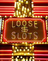 Bright neon lights display the words 'Loose Slots' with a dollar sign in the center. The sign is outlined with bulbs, creating a vibrant and flashy effect typical of a casino or entertainment venue.